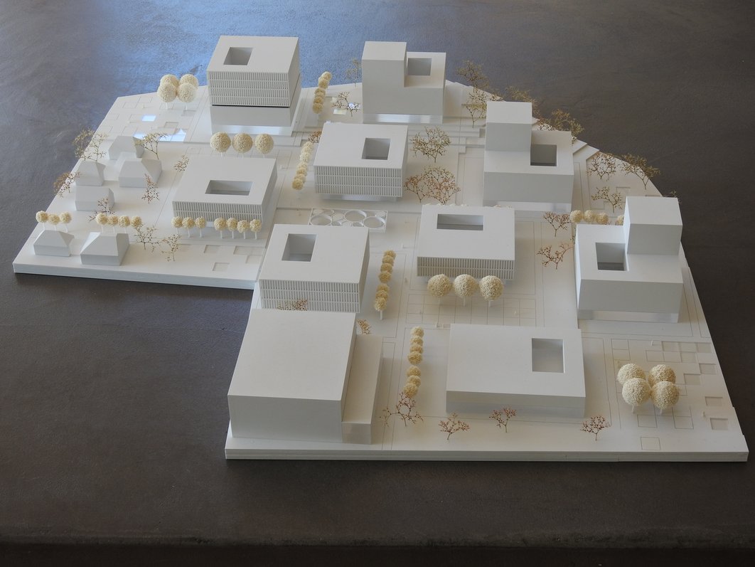 In weiß gehaltenes 3-D-Modell mit einzelnen Gebäuden, die in größerem Abstand zueinander und mit Wegen dazwischen angeordnet sind. Alle haben fast quadratische Grundflächen, jedoch unterschiedlich hoch sind. Jedes Gebäude hat asymmetrisch angeordnete Innenhöfe