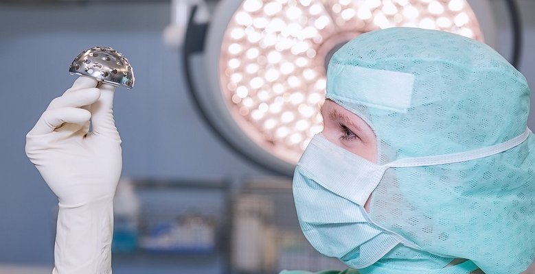 Frau in OP-Kleidung hält ein medizinisches Gerät in den Händen und schaut es sich genau an