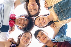 The camera is on the ground and is pointing towards the sky. Five young people stretch their heads into the picture.