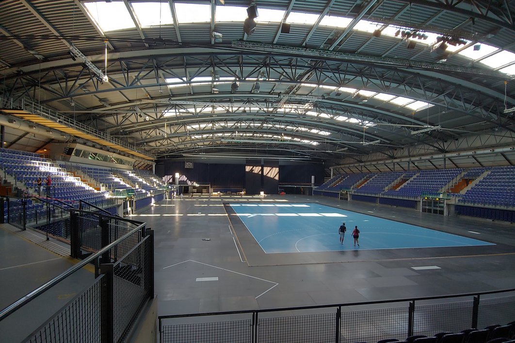 Innenaufnahme der leeren QUARTERBACK Immobilien Arena Leipzig. Auf der Sportfläche sind zwei Menschen zu sehen.