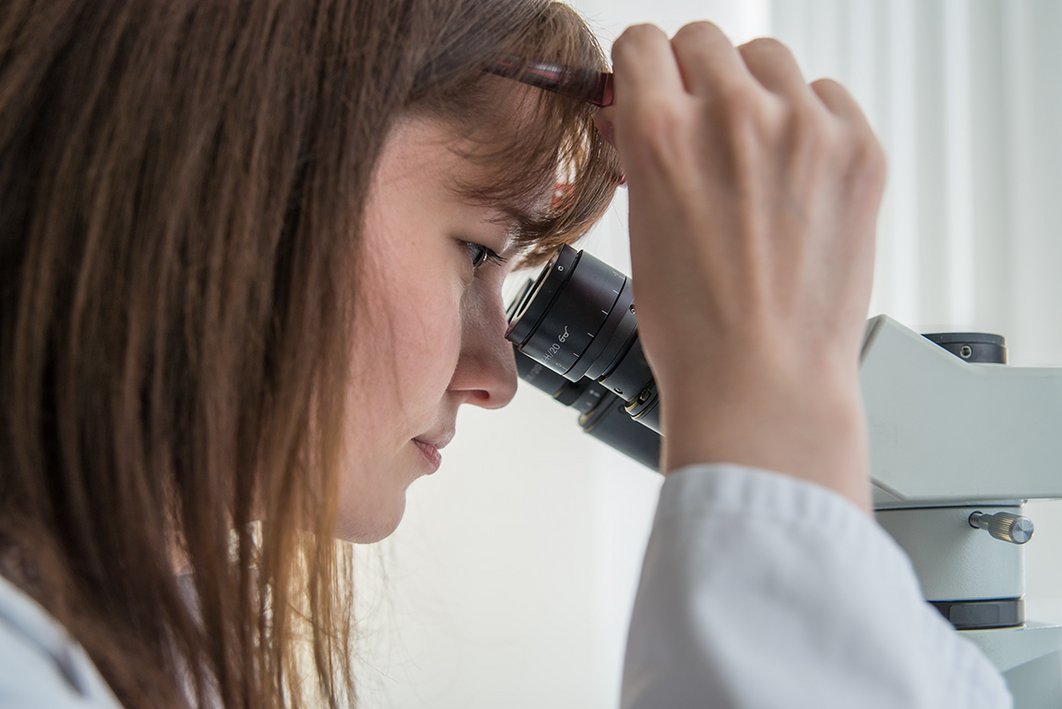Eine Mitarbeiterin betrachtet etwas durch ein Mikroskop.