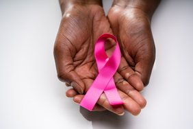 Eine Rose Schleife als internationales Symbol für Brustkrebs in den Händen eines Schwarzen Menschen. 