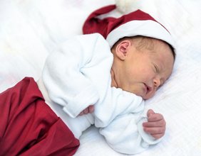 Neugeborenes Baby mit Weihnachtsmannmütze und roter Hose.