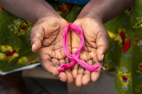 Eine Person hält ihre Handflächen in die Kamera. Darin befindet sich eine rosa Schleife aus Garn - ein Symbol, dass auf Brustkrebs aufmerksam machen soll.