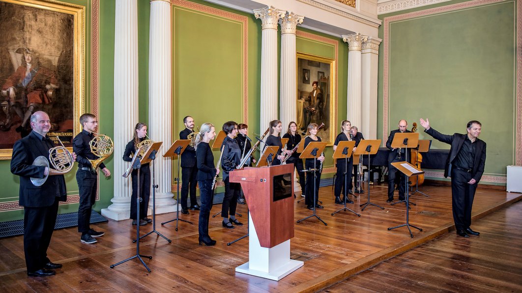 Eine Gruppe aus 14 Musiker:innen steht in der Aula des Löwengebäudes.