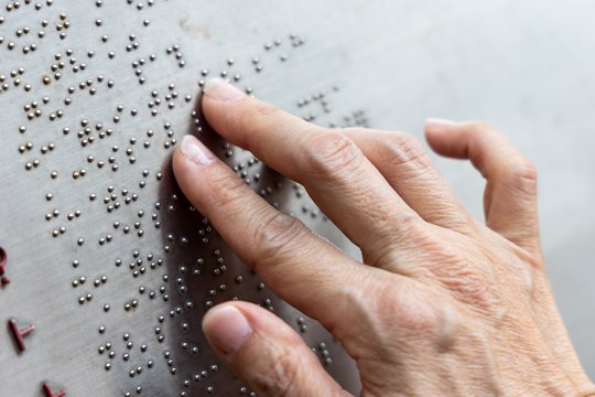 Finger lesen einen Text in Brailleschrift auf einer Info-Tafel