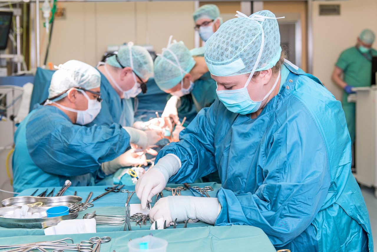 Laufende Operation. Im Vordergrund liegen sterile OP-Geräte. Fünf Mitarbietende kümmern sich um den Patienten.
