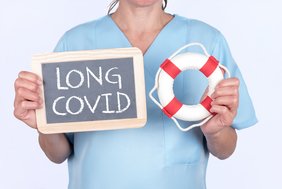 Eine Person in hellblauer medizinscher Arbeitskleidung hält rechts einen Rettungsreifen und links eine Tafel auf der Long Covid steht. Der Kopf der Person ist vom Bildrand abgeschnitten. 