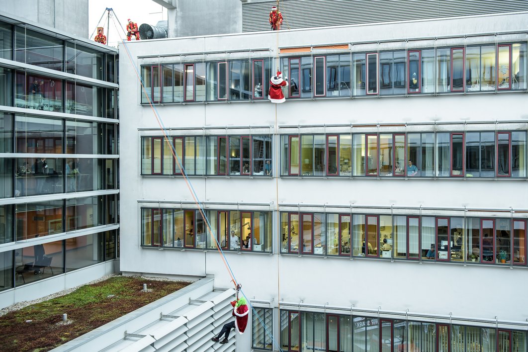 Die verkleideteten Mitarbeiter der Feuerwehr seilen sich vom Universitätsklinikum Halle (Saale) ab. An den Fenstern stehen Zuschauer:innen.