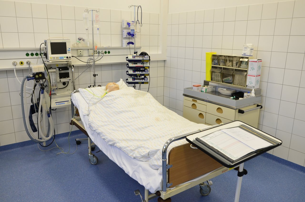 Krankenhausbett mit medizinischen Geräten drumherum; in dem Bett liegt eine Dummy-Puppe.