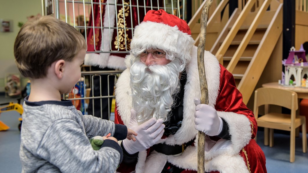 Ein als Weihnachtsmann verkleideter Mitarbeiter der Feuerwehr gibt einem kleinen Kind ein Geschenk.