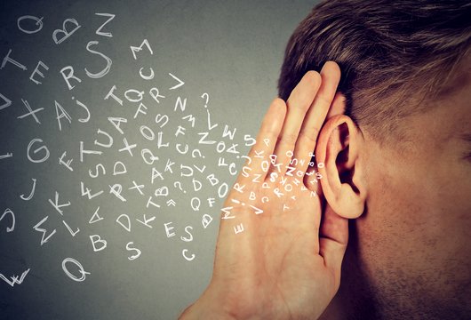 Rechts im Bild ist angeschnitten der Kopf einer Person zu sehen, die eine Hand hinter ihr Ohr hält, als würde sie lauschen. Von links fliegen viele einzelne Buchstaben auf das Ohr zu.